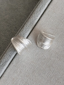Macro view showing brushed matte silver C-shaped earrings with textured wavy surface