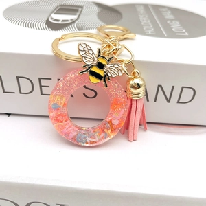 Close-up of pink resin letter O keychain with glitter, enamel bee, and leather tassel