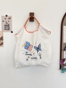 Detail of embroidered white tote bag with woven handles and vintage butterfly illustration