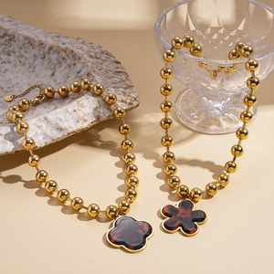 Vintage gold beaded necklace with clover pendant on stone tray with warm lighting