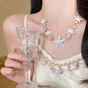 Detail of beach-style necklace featuring starfish, shell and pearls on a gold chain
