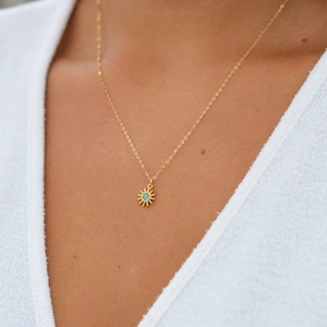 Detail of a golden sunflower necklace with turquoise stones worn on a white knit top