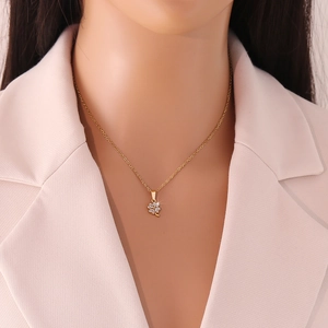 Detail eines goldenen Kleeblatt-Anhängers mit Zirkonia an einem Modell im rosa Anzug