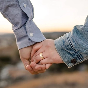 Close-up of golden matte wedding ring on hands with a warm sunset background