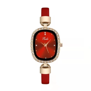 Detailansicht der ovalen Golduhr mit rotem Lederarmband und glitzernder Strass-Lünette