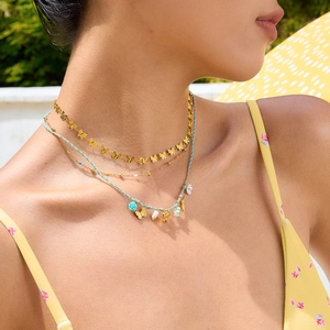 Close-up of gold butterfly chain and turquoise braided necklace worn by model