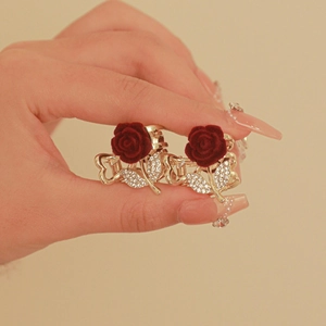 Close-up of golden metal hair clips with burgundy flocked roses and sparkling rhinestones