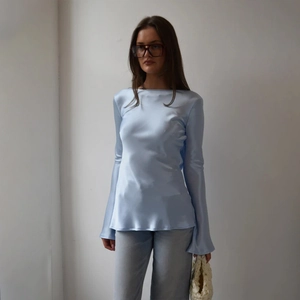 Détail du haut élégant en satin bleu clair avec manches longues évasées et dos ouvert chic
