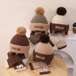 Detail of baby knitted hat and scarf set with fur pom-poms and hello embroidery