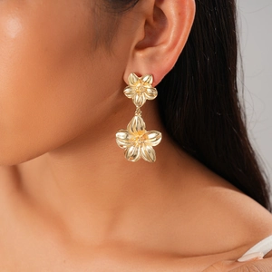 Close-up of dangling gold flower earrings with a polished metallic finish on a model