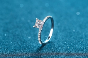 Macro shot of princess cut moissanite ring with side stones on blue starlight background