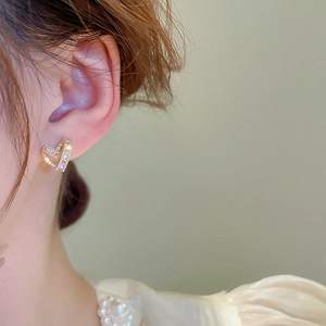 Close-up of a gold heart stud earring with cubic zirconia worn by a female model
