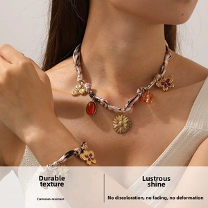 Détail du bracelet chaîne en ruban et collier avec pendentifs fleur et papillon