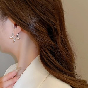 Close-up of elegant silver star-shaped metal earrings worn on a woman's earlobe