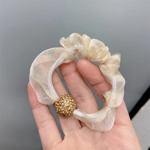 Detail of beige sheer mesh scrunchie with a sparkling gold glitter ball ornament