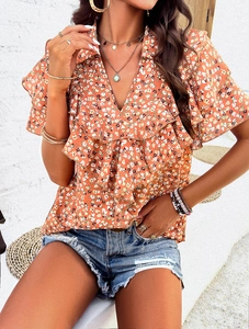 Detail of elegant V-neck floral top with ruffle sleeves and yellow print on orange fabric