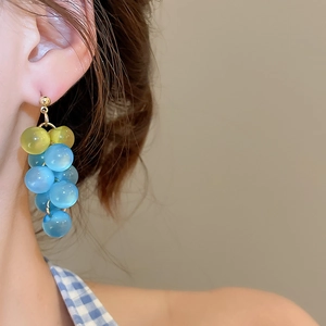 Detail of model wearing resin grape cluster drop earrings in sky blue and green