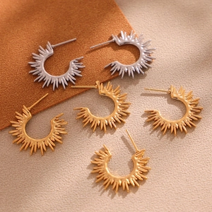 Fashionable 18K gold and silver sunflower sunburst C-shaped earrings on textured backdrop