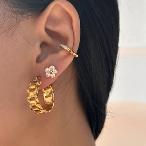 Macro shot of gold-plated chain hoop, flower stud and zircon ear cuff set on ear