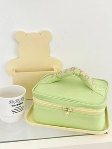 Quilted light green makeup bag with pink embroidery and top handle on display tray