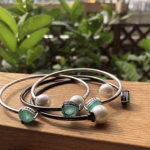 Detail of silver open bangle featuring white pearls and faceted green gemstones