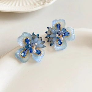 Détail des boucles d'oreilles fleurs bleues avec cristaux et perles sur plateau blanc