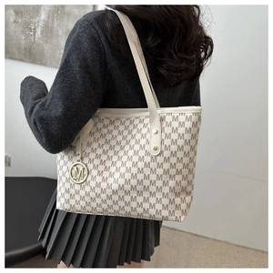 Detail of beige monogram tote bag with gold M charm and elegant leather shoulder strap