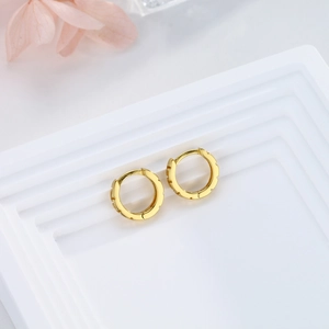 Macro shot of gold hoop earrings with textured gear edges on a white geometric stand