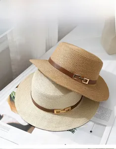 Close-up of woven straw hats with leather bands and gold chain buckles on a magazine