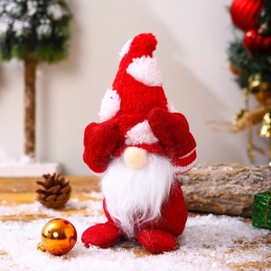 Detail of red and white plush Christmas gnome with festive tree and snow background