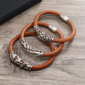 Three braided brown leather bracelets with silver dragon and leaf charms on wood