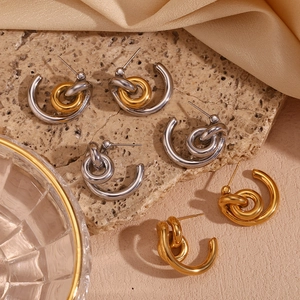 Three pairs of twisted knot C-shaped earrings in gold and silver finish on a stone plate