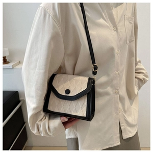 Detail view of beige canvas crossbody bag with black leather trim and quilted diamond texture