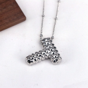 Macro detail of silver letter T pendant necklace with unique studded texture on white fabric