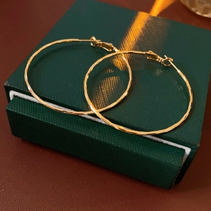 Détail de grandes créoles plaquées or avec texture martelée sur un coffret vert chic