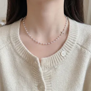 Elegant pearl necklace with a minimalist silver cross pendant shown on a female neck