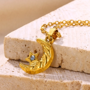 Close-up of 18K gold star and moon pendant with a blue zircon inlay on textured stone