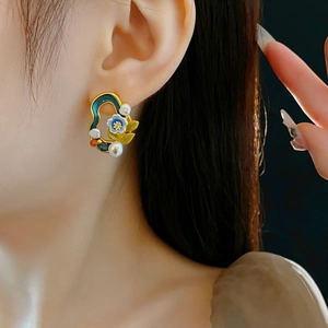 Close-up of vintage gold floral earrings with green enamel and pearls worn by a model
