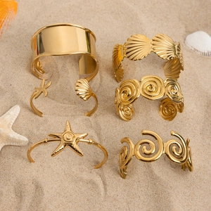 Detail view of 18K gold plated ocean starfish and wave bangles set on a sandy beach