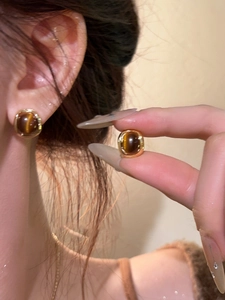 Macro detail of 18k gold plated oval tiger eye earrings shown on a model's ear