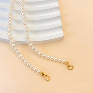 Elegant imitation pearl necklace with gold clasp on white minimalist steps