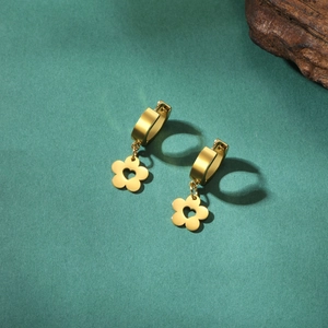 Detail shot of gold flower earrings with heart cutout on a textured green background