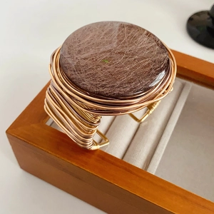 Macro view of wide handmade wire wrapped gold bracelet featuring a large round resin stone