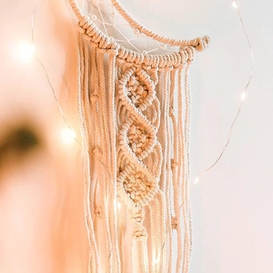 Handwoven macrame dreamcatcher with tassels and warm LED lights on a white wall