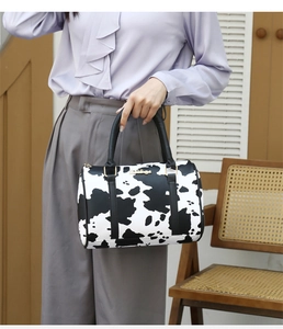 Detail of a cow print Boston bag featuring black handles and gold hardware accents