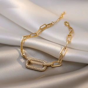 Close-up of gold chain bracelet with zircon geometric rectangle on silk background