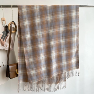 Detailed close-up of brown and blue plaid cashmere-like scarf with fringe hanging on a rack