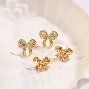 Close-up of golden bow-shaped stud earrings with pink teardrop gems and clear crystals