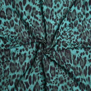 Détail du tissu en satin vert à motif léopard avec une texture soyeuse et brillante