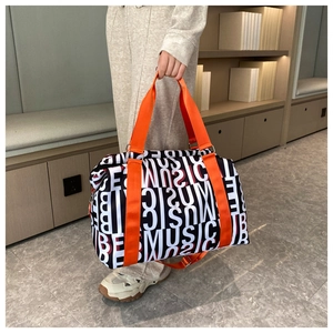 Detail of travel bag featuring red and white letter patterns and orange woven handles